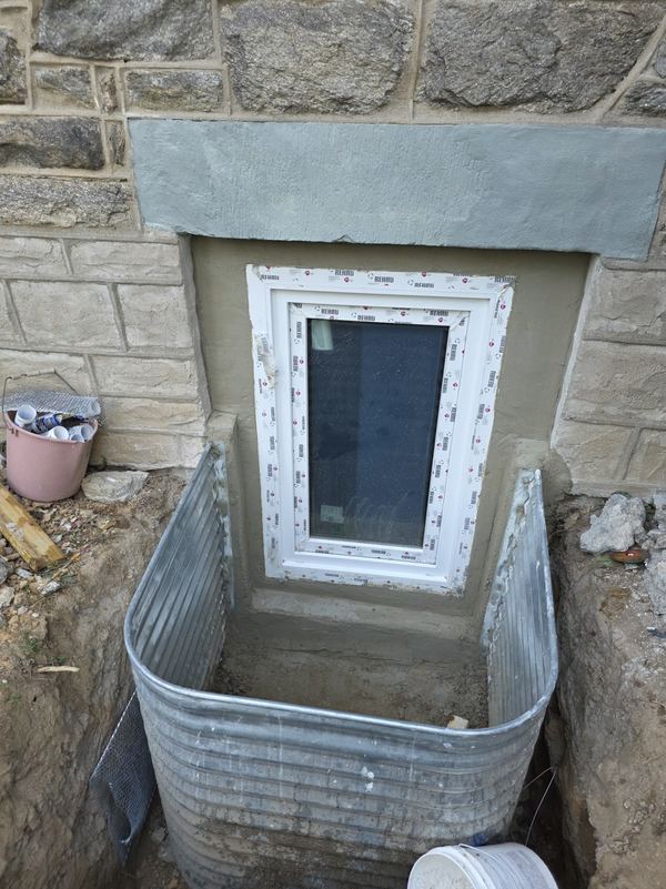 Finished basement egress window with steel window well in a stone foundation
