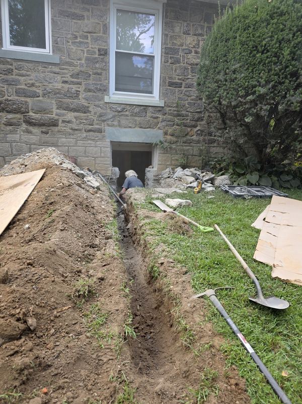 Trench excavated along a stone foundation for a new basement egress window