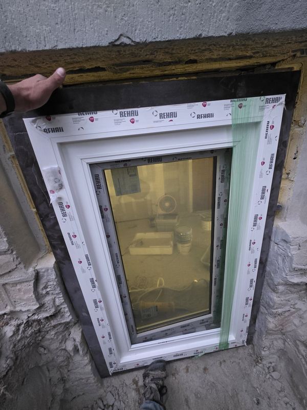 New egress window being set into a cut opening in a stone foundation wall